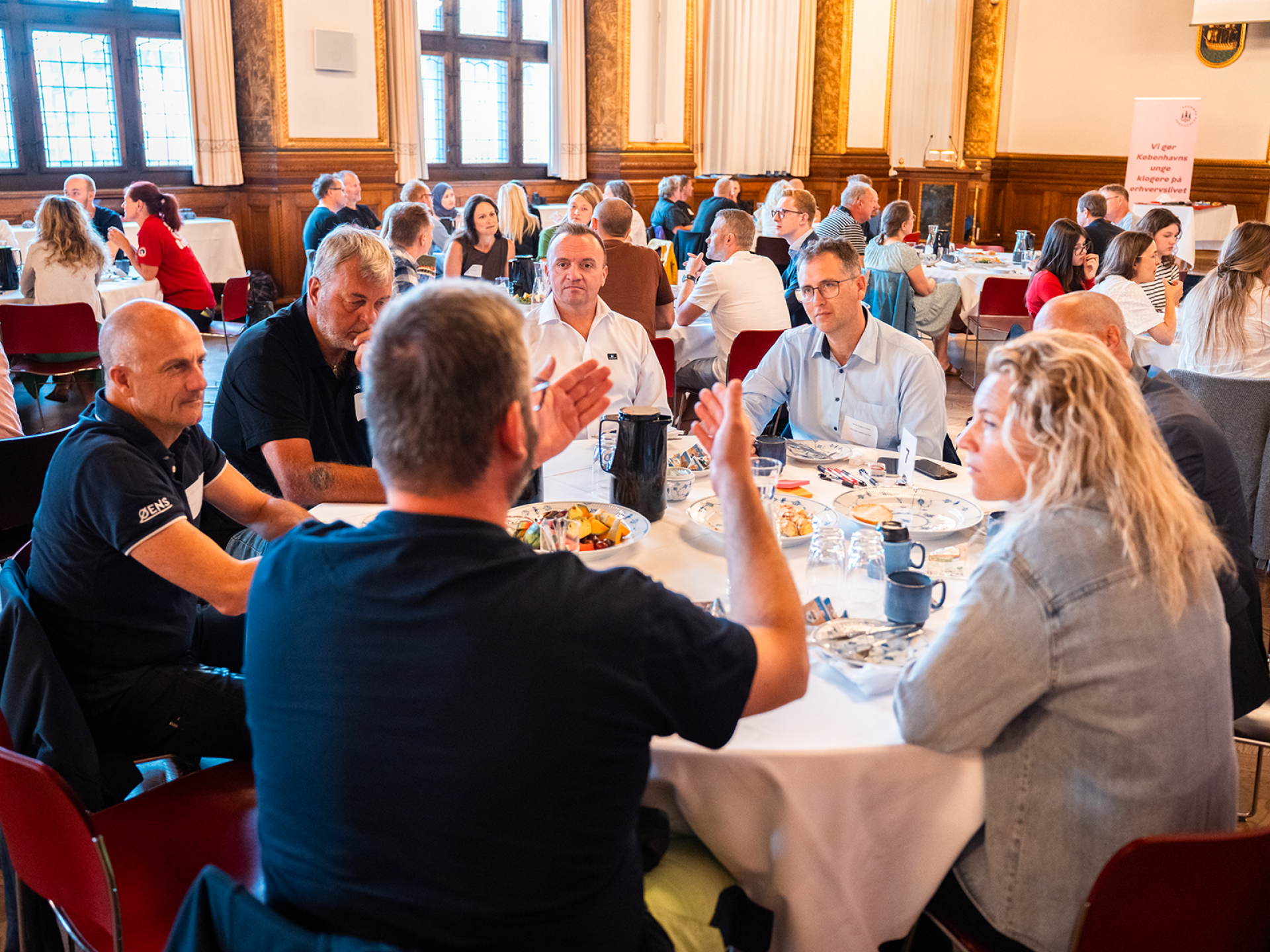 Mennesker sidder ved runde borde i stor sal